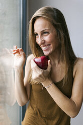 Woman standing by window, eating apple - VABF00900