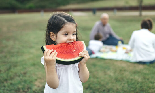 Mädchen isst Wassermelonenscheibe mit ihrer Familie im Hintergrund - DAPF00523