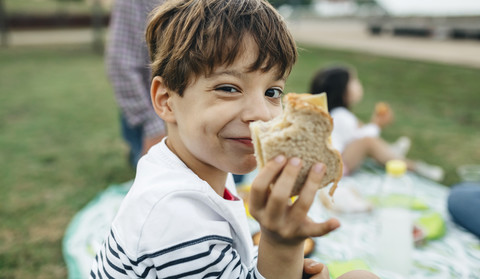 Portrait of smiling boy holding sandwich with his family in background stock photo