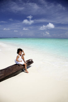 Malediven, Mädchen sitzt auf einem Baumstamm am Strand - DSGF01244