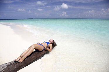 Malediven, Frau beim Sonnenbad auf einem Baumstamm am Strand - DSGF01245