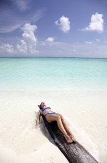 Malediven, Frau beim Sonnenbad auf einem Baumstamm am Strand - DSGF01246