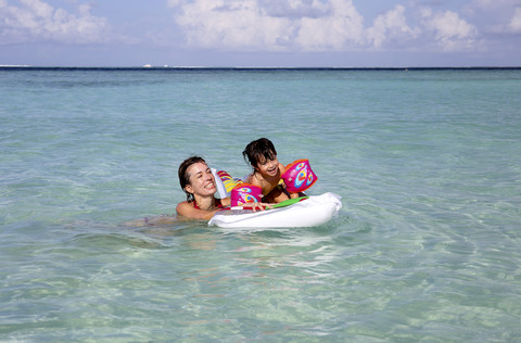 Malediven, Gulhi, Mutter und Tochter spielen mit einer aufblasbaren Luftmatratze im seichten Wasser, lizenzfreies Stockfoto