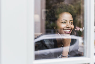 Smiling young woman looking out of window - UUF09486