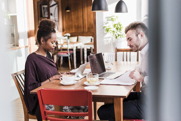 Junger Mann und Frau benutzen Laptop und Tablet in einem Café - UUF09495