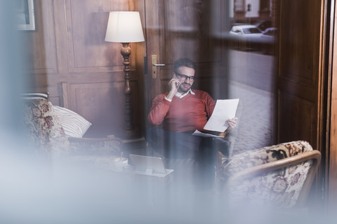 Junger Mann mit Handy, der ein Dokument in einem Café betrachtet, lizenzfreies Stockfoto