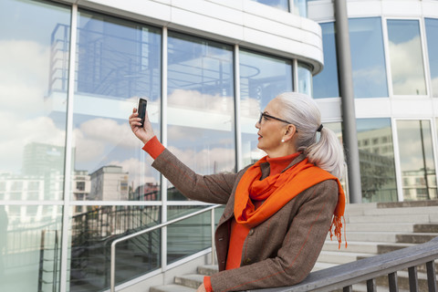 Fashionable mature woman taking selfie with cell phone stock photo