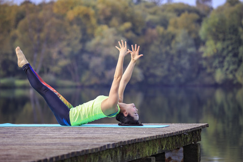 Frau übt Yoga auf einem Steg an einem See, lizenzfreies Stockfoto