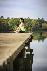 Woman practicing yoga on jetty at a lake - VTF00570