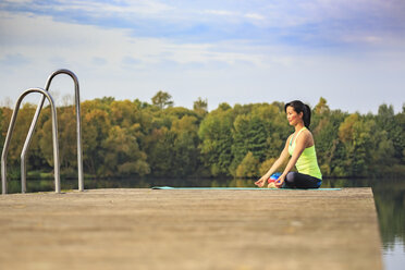 Woman practicing yoga on jetty at a lake - VTF00571