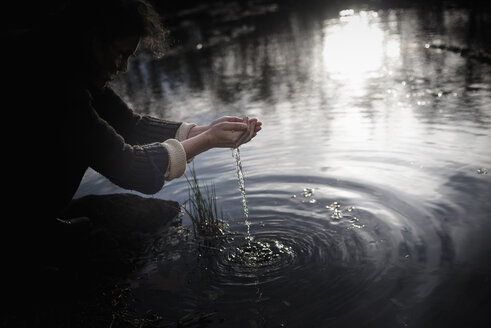 Woman crouching at water's edge scooping water - MJF02118