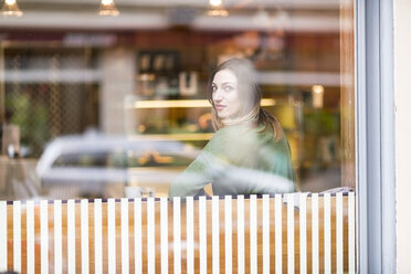 Junge Frau sitzt in einem Café und schaut durch das Fenster - TAMF00892