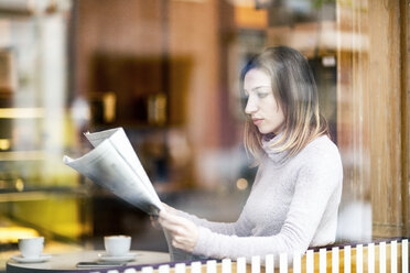 Junge Frau sitzt in einem Café und liest Zeitung - TAMF00894