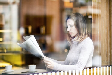 Young woman sitting in coffee shop, reading newspaper - TAMF00894