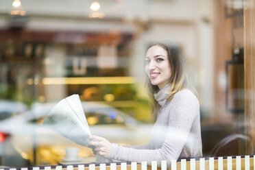 Young woman sitting in coffee shop, reading newspaper - TAMF00895