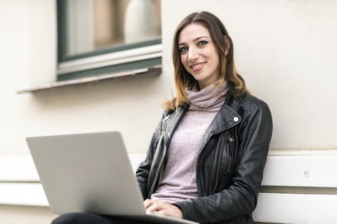 Junge Frau sitzt auf einer Bank im Freien und benutzt einen Laptop, lizenzfreies Stockfoto