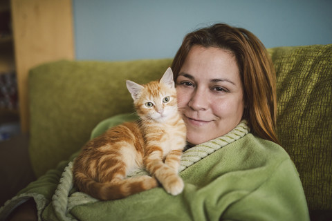 Portrait of happy woman with her kitten on the couch at home stock photo