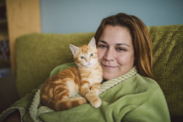 Portrait of happy woman with her kitten on the couch at home - RAEF01597