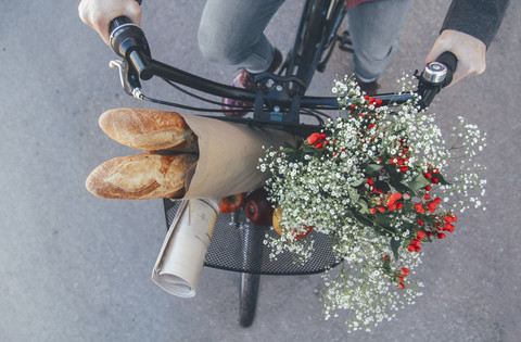 Mann mit Äpfeln, Blumenstrauß, Zeitung und Baguette im Fahrradkorb, lizenzfreies Stockfoto