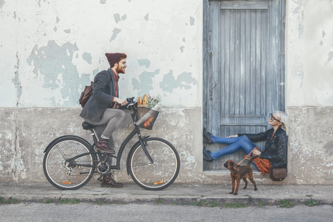 Young man on bicycle smiling at woman with dog stock photo