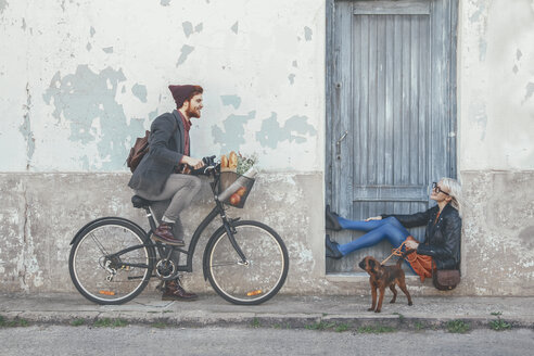 Young man on bicycle smiling at woman with dog - RTBF00558