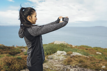 Ireland, Howth, female athlete taking cell phone picture at cliff coast - MADF01298