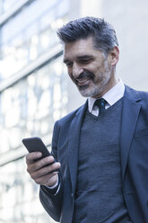 Smiling businessman outdoors looking on cell phone - TCF05213