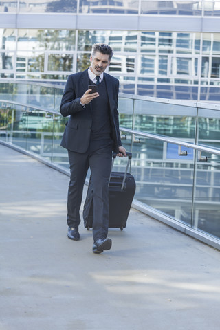 Businessman with cell phone walking with suitcase on bridge stock photo