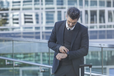 Businessman standing on bridge checking the time - TCF05231