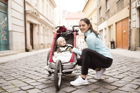 Mutter in Sportkleidung mit Kind im Kinderwagen in der Stadt, lizenzfreies Stockfoto