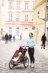 Mutter in Sportkleidung mit Kind im Kinderwagen in der Stadt - HAPF01206