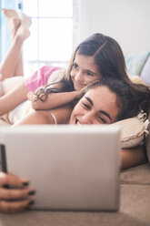 Teenage girl and her little sister lying on couch using tablet - SIPF01170