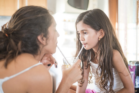 Teenager-Mädchen und ihre kleine Schwester in der Küche teilen sich ein Getränk, lizenzfreies Stockfoto