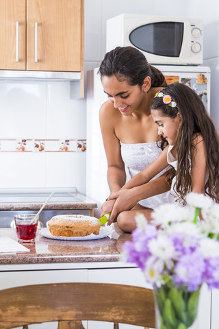 Teenager-Mädchen und ihre kleine Schwester in der Küche schneiden einen Kuchen, lizenzfreies Stockfoto