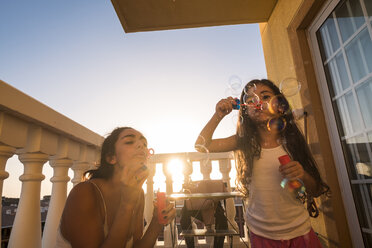 Teenage girl and her little sister blowing soap bubbles on balcony - SIPF01187