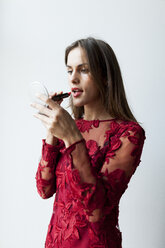 Schöne junge Frau im roten Kleid trägt Lippenstift auf - VABF00919
