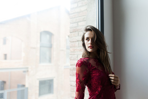 Schöne junge Frau in rotem Kleid vor einem Fenster, lizenzfreies Stockfoto