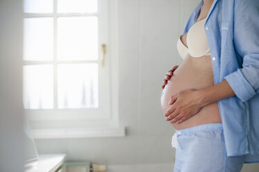Pregnant woman holding her belly in bathroom - DIGF01494