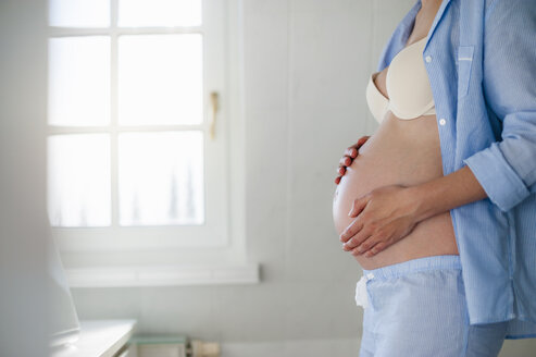 Schwangere Frau hält ihren Bauch im Badezimmer - DIGF01494