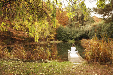 Man sitting on a jetty at a pond in autumn - MFRF00829