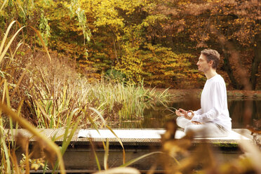 Man practicing yoga on a jetty at a pond in autumn - MFRF00831