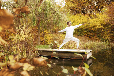 Mann übt Yoga auf einem Steg an einem Teich im Herbst - MFRF00833