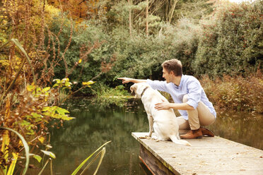 Mann mit Hund auf einem Steg an einem Teich im Herbst - MFRF00835
