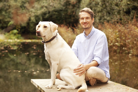 Mann mit Hund auf einem Steg an einem Teich im Herbst, lizenzfreies Stockfoto