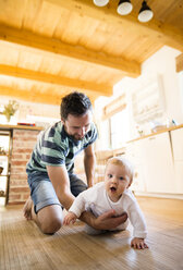 Father supporting crawling baby at home - HAPF01214