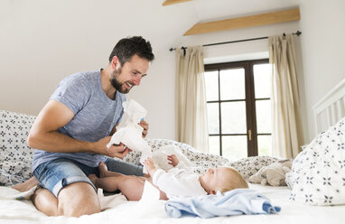Father changing baby's diapers on bed - HAPF01216