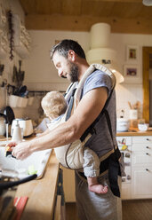 Happy father with baby in baby carrier doing the dishes - HAPF01223