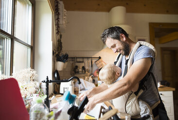 Happy father with baby in baby carrier doing the dishes - HAPF01224