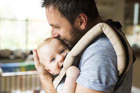 Glücklicher Vater mit Baby im Tragesitz zu Hause, lizenzfreies Stockfoto