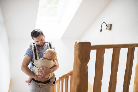 Vater mit Baby im Tragesack geht die Treppe hinauf, lizenzfreies Stockfoto